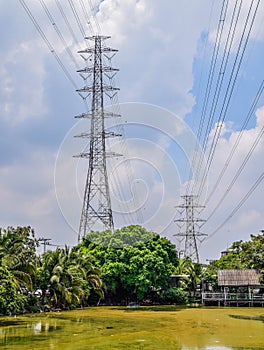 Two high voltage power poles located among the trees along the large ponds and restaurants in city,  High voltage electric poles