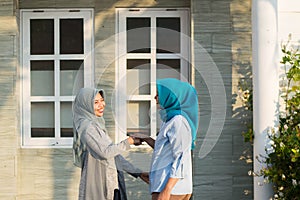 Two hijab women neighbors meet and say hi while smiling and shake hands in front of their house