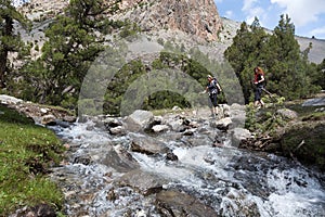 Two hikers crossing fast flowing river