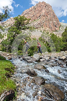 Two hikers crossing fast flowing river