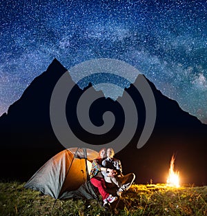 Two hikers having a rest in his camp at night near campfire under shines starry sky