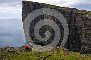 Two hikers sitting on the edge of a cliff on Faroe Islands