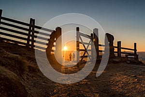 Two hikers stunning dawn sunrise in mountain hills hiker climber climbing wooden fence style silhouette with open gate