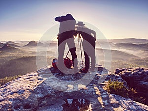 Two hikers taking pictures and talk on top of mountain. Two photographers