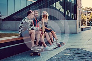 Two hipster males and blond female with longboards resting.