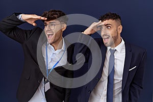 Two hispanic business men wearing business clothes very happy and smiling looking far away with hand over head