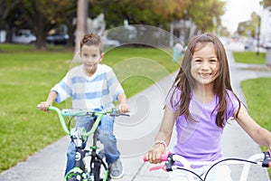 Two Hispanic Children Riding Bikes In Park