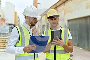 Two hispanic men architects reading document using touchpad at street