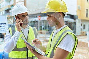 Two hispanic men architects writing on document talking on smartphone at street