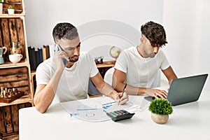 Two hispanic men couple talking on the smartphone and using laptop working at home