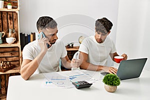 Two hispanic men couple talking on the smartphone and using laptop working at home