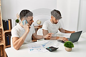 Two hispanic men couple talking on the smartphone and using laptop working at home