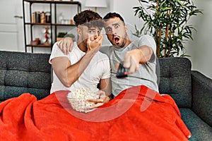 Two hispanic men couple watching movie sitting on sofa at home