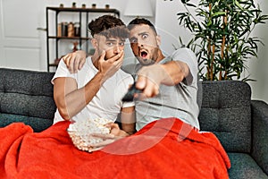 Two hispanic men couple watching movie sitting on sofa at home