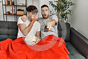 Two hispanic men couple watching movie sitting on sofa at home