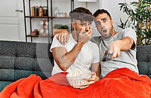 Two hispanic men couple watching movie sitting on sofa at home