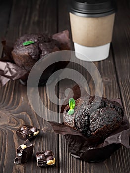 Two homemade chocolate muffin, decorated leaf mint on a dark wooden table. Paper cup with tea or coffee. Near chocolate slices.