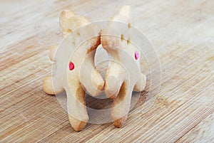 Two homemade cookies in the form of bear cubs standing hand in hand against the background of a wooden board