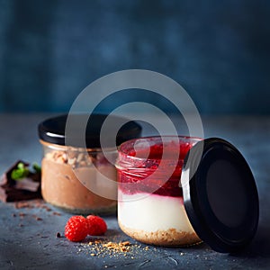 Two homemade easy cheesecakes in jars with chocolate mousse and raspberry curd sauce on a dark blue background. Healthy dessert.