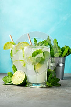Two homemade lemonade or mojito cocktail with lime, mint and ice cubes in a glass on a light stone table. Fresh summer