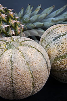 Two honeydews and a fresh pineapple on a black surface.