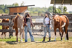 Two horse-riding girls discuss horses on a ranch while standing next to them