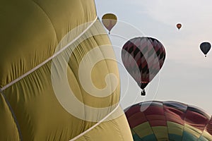 Two hot air balloons inflate side-by-side as four more fly in the background