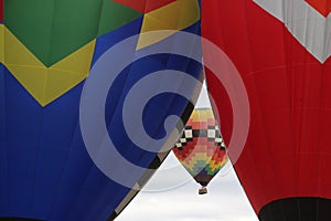 Two hot air balloons inflate side-by-side as a third flies in the background