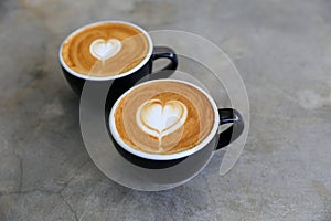 Two hot cups of cappucino on concrete background. Heart shape art latte symbol of love
