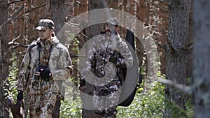 Two hunter men in camouflage clothes with guns walking through forest during hunting season. Man hunter outdoor in