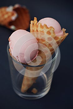 Two Ice cream in waffle cone with scoop of pink fruit ice cream and confetti in glass isolated on dark blue background