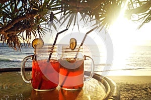 Two iced tea cocktails on table on background of palm trees at sunset