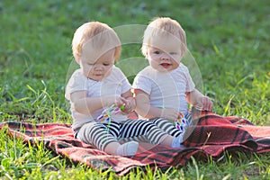 Two identical girls on a blanket in park look in surprise