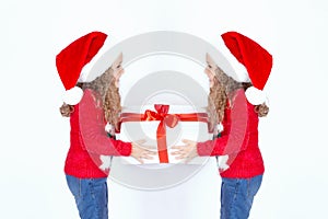 Two identical little twin girls in Santa Christmas hats hold a white box with a gift on a white background.