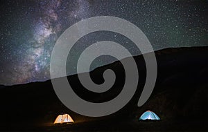 Two illuminated tents in the mountains against the backdrop of the milky way