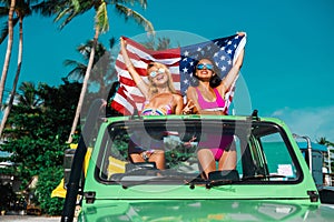 Two incredible beautiful young girls in bikini swimsuits, traveling around a tropical island in a car cabriolet off-road, in hands