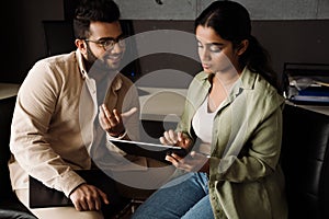 Two indian colleagues discussing business details and using tablet while sitting in office