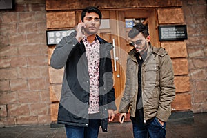 Two indian guys on jackets posed outdoor against door of pub