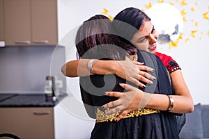 two indian women with bindi on the forehead hugging in living room photo