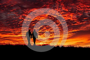 Two individuals standing together in a grassy field, A romantic silhouette of two figures walking hand in hand against a fiery