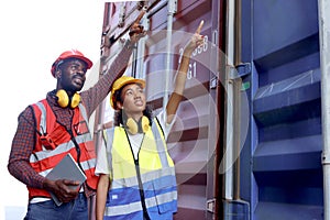 Two industrial African American engineer man and woman wearing safety vest and helmet working together at logistic shipping cargo