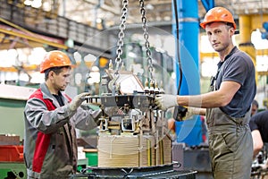 Two industrial workers assembling power transformer at conveyor factory workshop