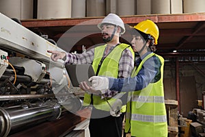 Two industrial workers use a laptop to check a paper manufacturing machine