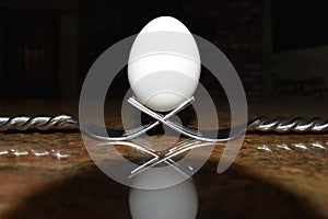 Two intertwined forks cradle a while egg in its center