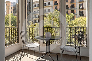 Two iron chairs and table on closed glazed terrace with beautiful view of cozy new area of warm country on sunny summer