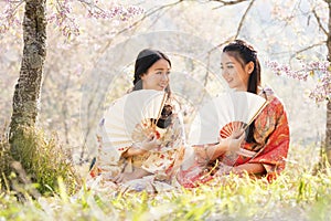 Two japanese girl wearing a kimono holding a white blow. Beautiful Female wearing traditional japanese kimono with cherry blossom
