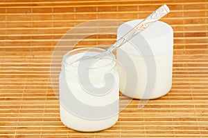 Two jars with home yoghurt and spoon on a straw mat