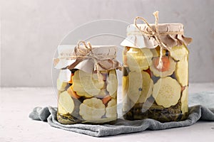 Two jars of pickleds patissons with cucumbers and carrots on light gray background, Closeup, Horizontal format