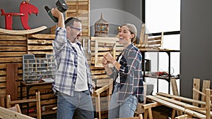 Two jaunty carpenters, a man and woman, dancing and drilling to music at their lively furniture carpentry business workplace