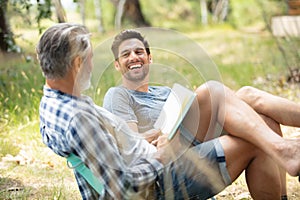 two jovial men relaxing in countryside with book